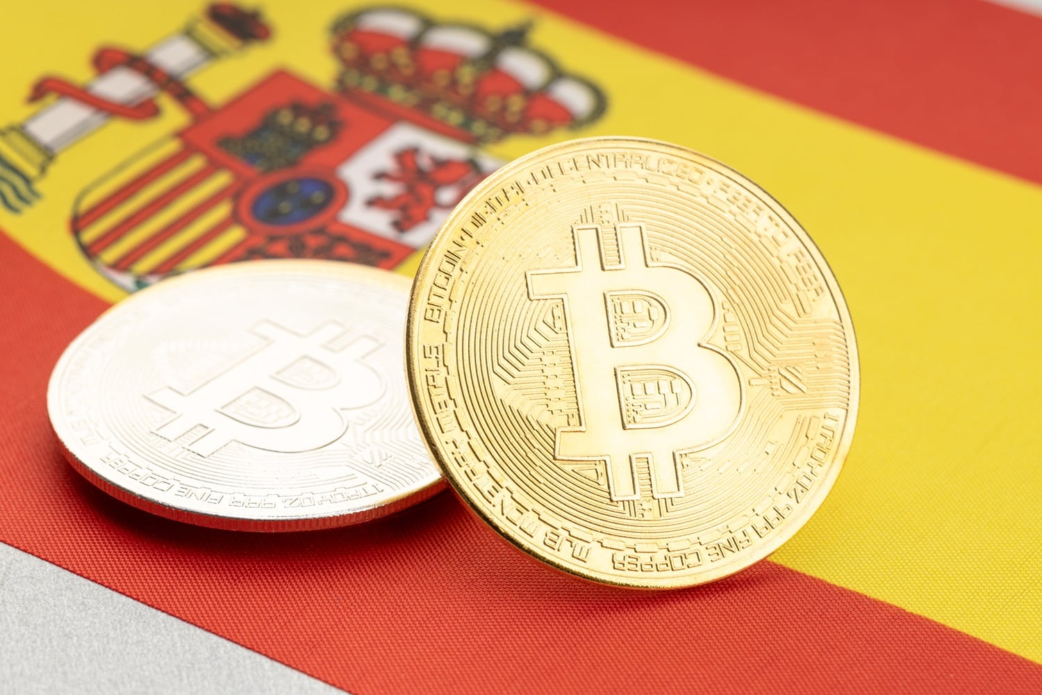 Metal coins intended to represent Bitcoin rest on the national flag of Spain.