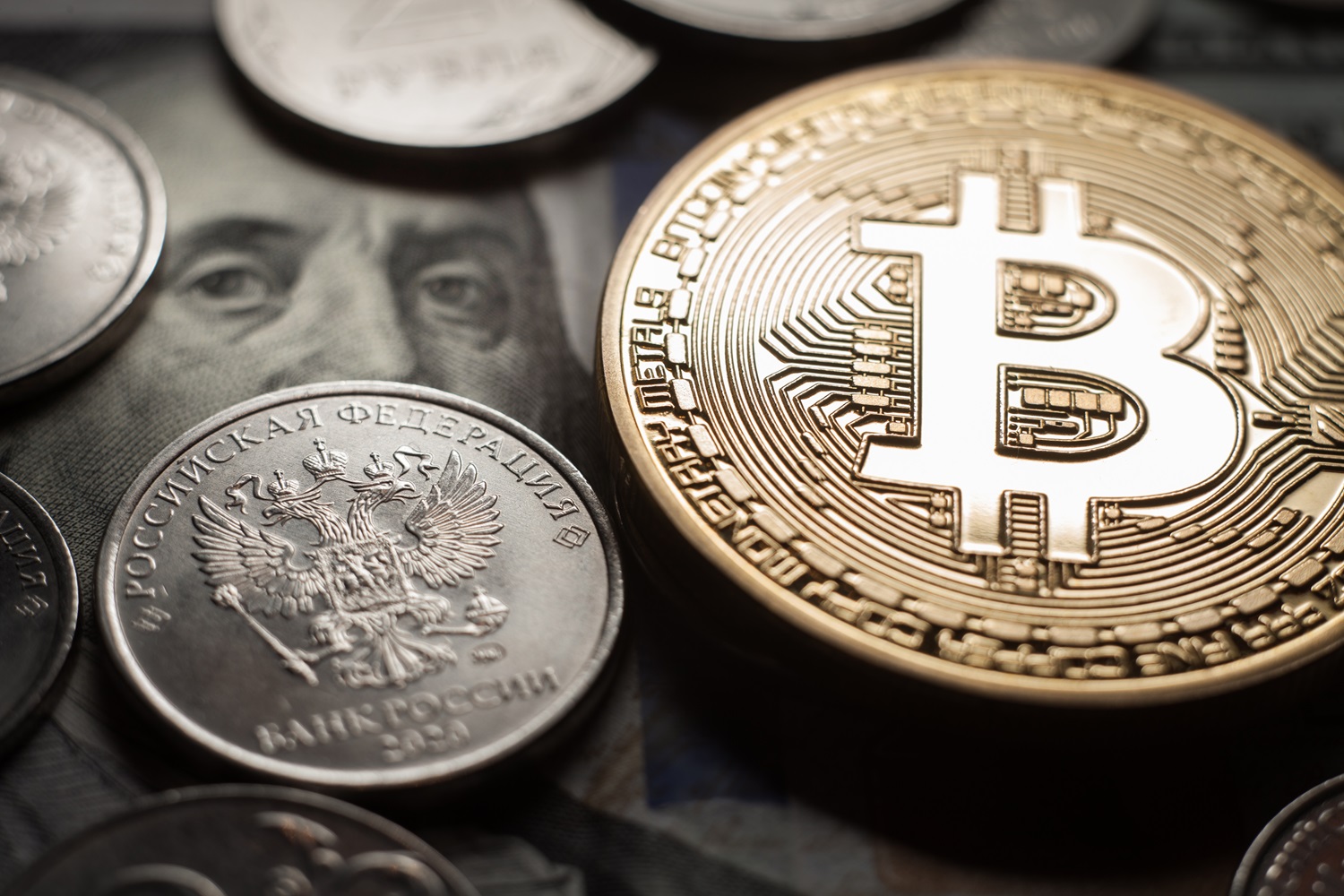 A metal coin intended to represent Bitcoin, next to Russian ruble coins and US dollar banknotes.