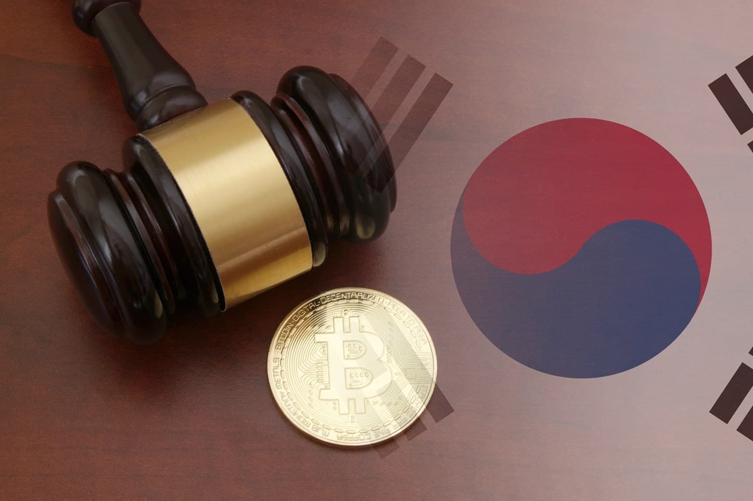 A judge’s gavel next to a metal coin intended to represent Bitcoin on a wooden table next to the South Korean flag.