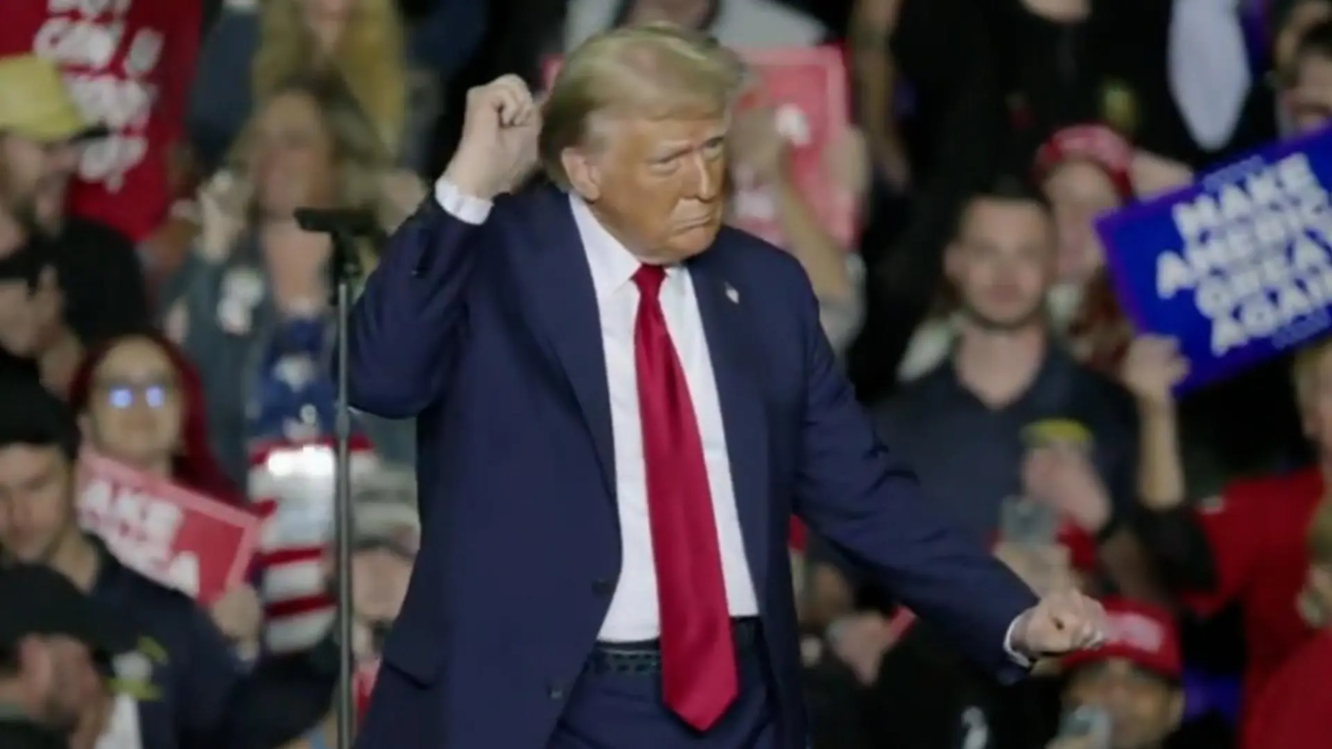 Donald Trump gestures at a campaign rally with supporters in the background.