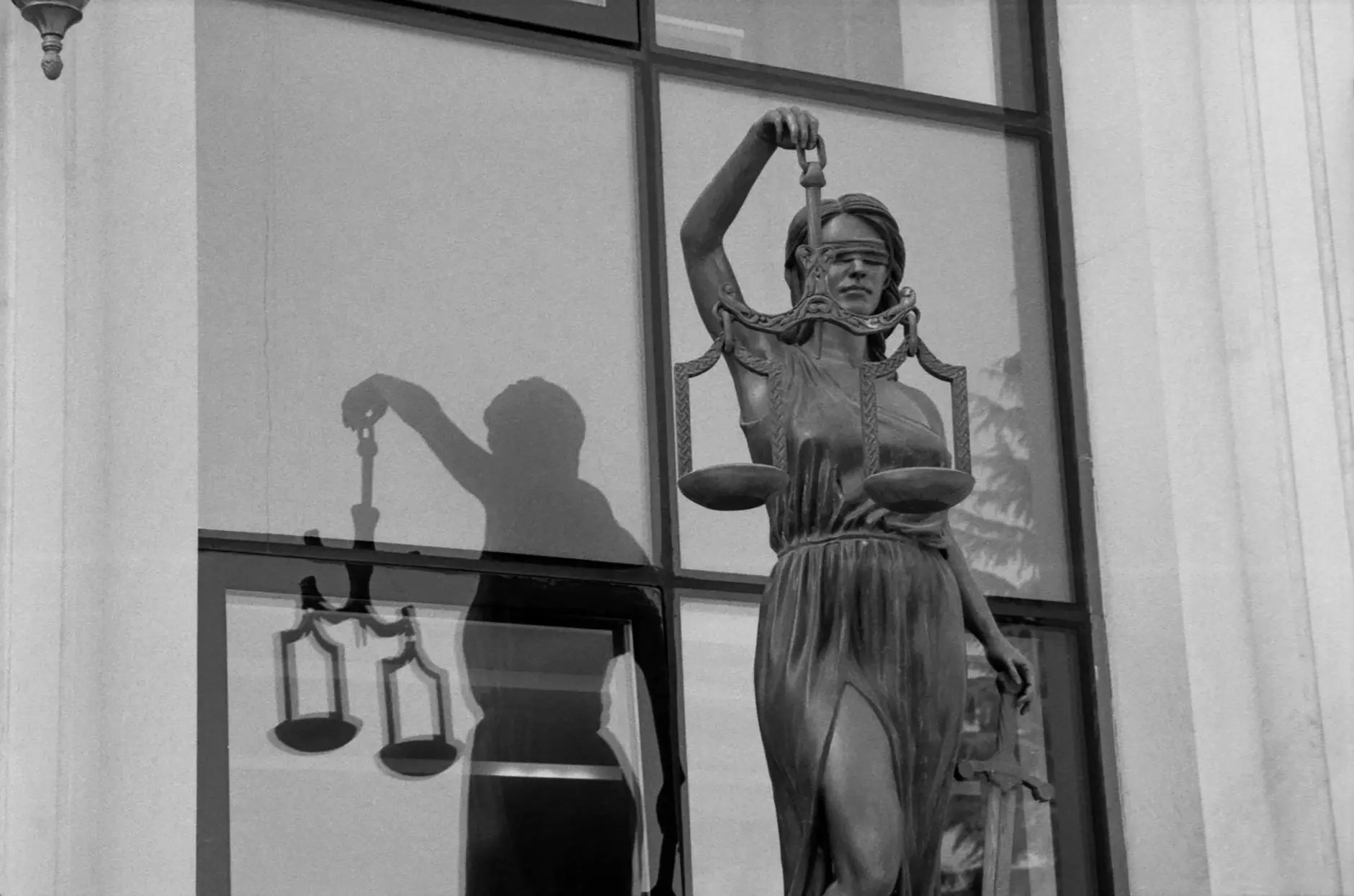 A statue of Lady Justice holding scales in front of a window.