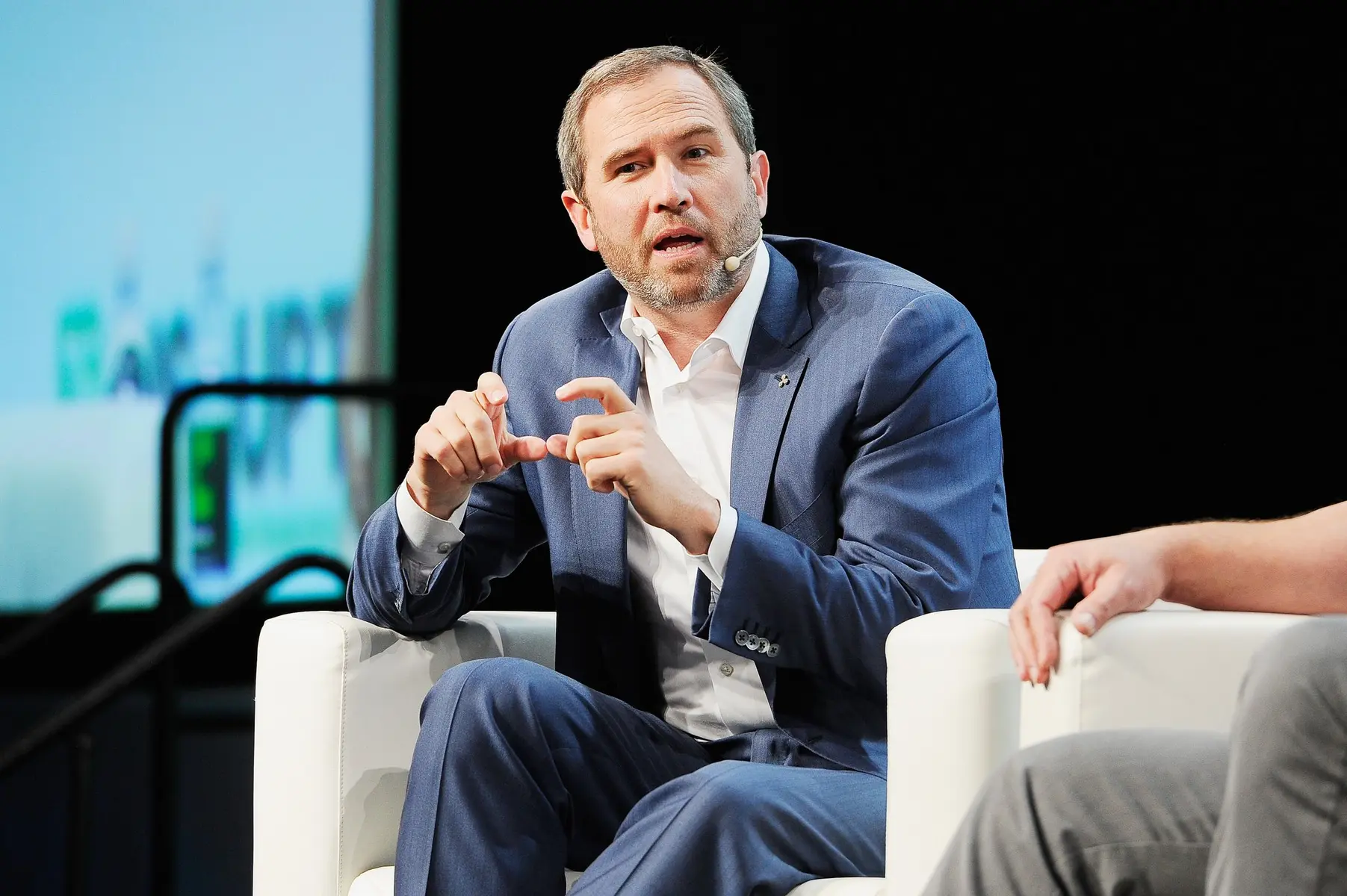 Brad Garlinghouse, CEO of Ripple, speaking while seated in a white armchair during a presentation.